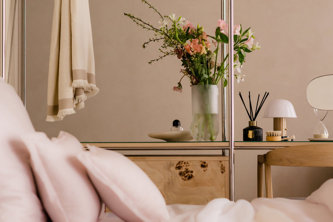 Elegantes Schlafzimmer mit rosafarbener AMQUA Bettwäsche, Blumen, Spiegel und warmem, neutralem Interieur.